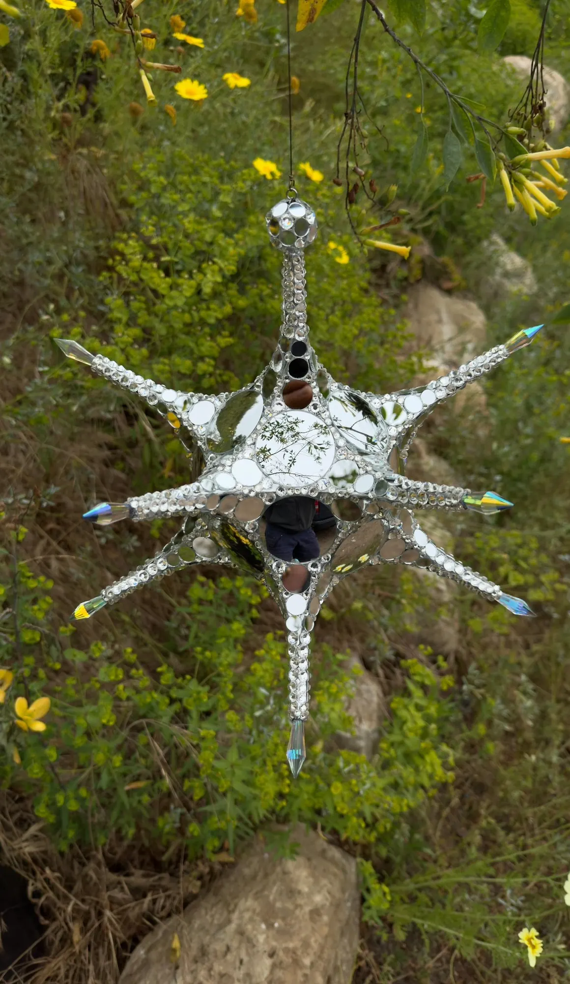 Metatron Reflections: a mirrored, rhinestone-set star sculpture with twelve points and crystal tips, hanging above green plants
